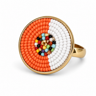 The image shows a circular ring featuring a vibrant design created with colorful beads. The ring has a gold-toned band that supports a circular face decorated with concentric patterns of orange, white, and various multicolored beads arranged in a spiral formation.