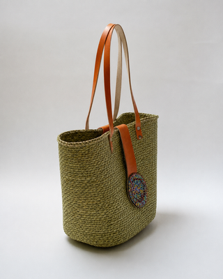 Woven Straw Kiondoo basket with two orange leather handles and a circular decorative patch featuring colorful beads on the front