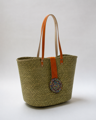 Woven Straw Kiondoo basket with two orange leather handles and a circular decorative patch featuring colorful beads on the front